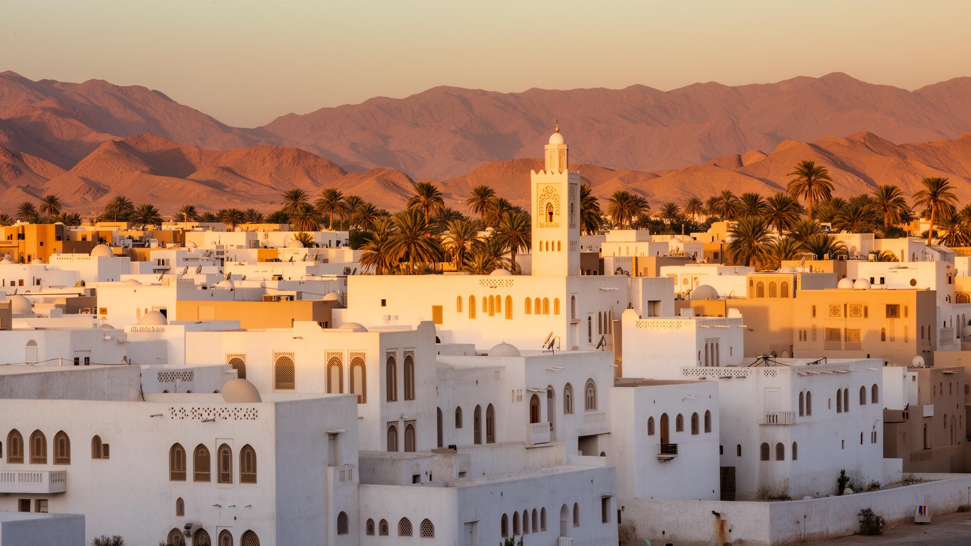 Traditionele witte Omaanse architectuur met minaret, palmen en Hajar bergen bij zonsondergang